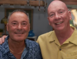 Two Caucasion men smiling side by side, one in a blue shirt, the other in yellow.