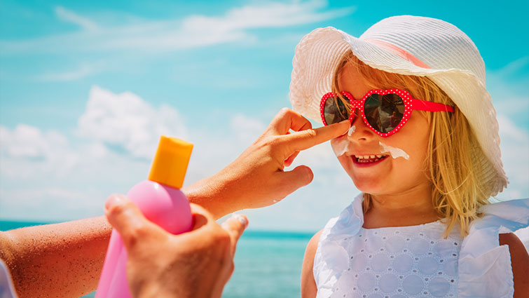 Parent putting sunscreen on child wearing sunglasses 