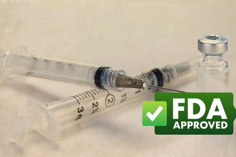 clear vaccine vial next to needle with green badge that says "FDA APPROVAL"