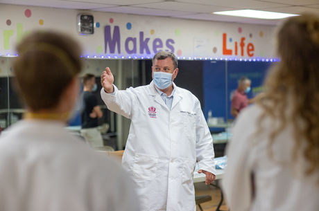 Caucasian doctor stands in white coat with hand outstretched guiding people.