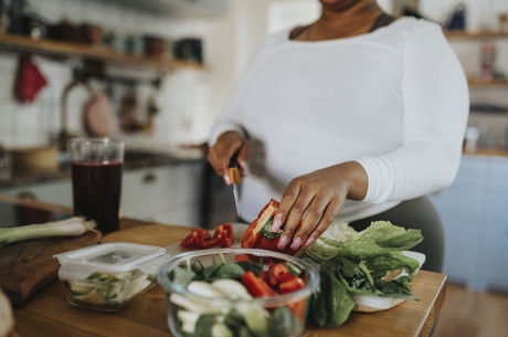 Midsection of young woman cutting red bell pepper while preparing salad in kitchen at home