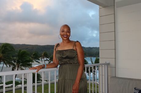 Sonja Loadholt stands on balcony overlooking beach and palm trees