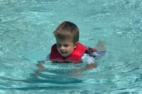 Young boy swims in pool with US Coast-guard approved life vest