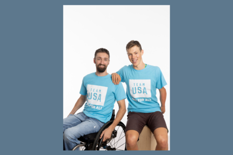 two Caucasion males, one in a wheelchair in blue t-shirts