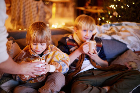 Two young boys sitting on a couch drinking hot chocolate 
