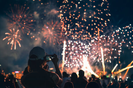  The back of a girl in a baseball cap filming a fireworks display on her mobile phone