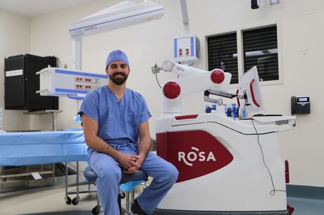 Doctor in blue scrubs sitting in front of a Rosa robot 