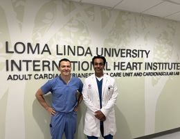 Dr. Mohsen stands left of Dr. Prasad in blue scrubs in front of LLU IHI signage