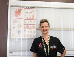 Dr. Rajfer stands next to a poster of the shoulders anatomy as she smiles at the camera