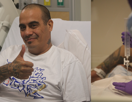 a man sitting in a hospital bed gives a thumbs up 