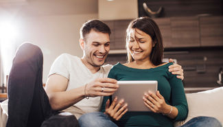 Couple on couch smiling looking at tablet