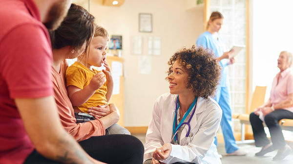 Female doctor kneeling to talk with parents of small child