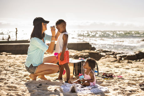 Mom putting suntan lotion on her little children at the beach stock photo