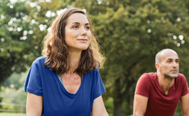 Woman in blue shirt outdoors with man in red shirt doing yoga