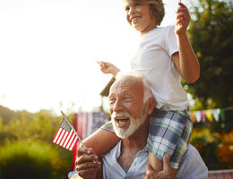 Boy on grandfathers shoulders holding American flag.