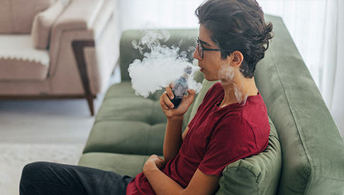 young adult sitting at a couch and vaping