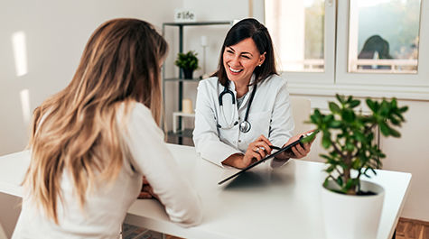 happy female doctor talking to female patient in an office looking at a clipboard